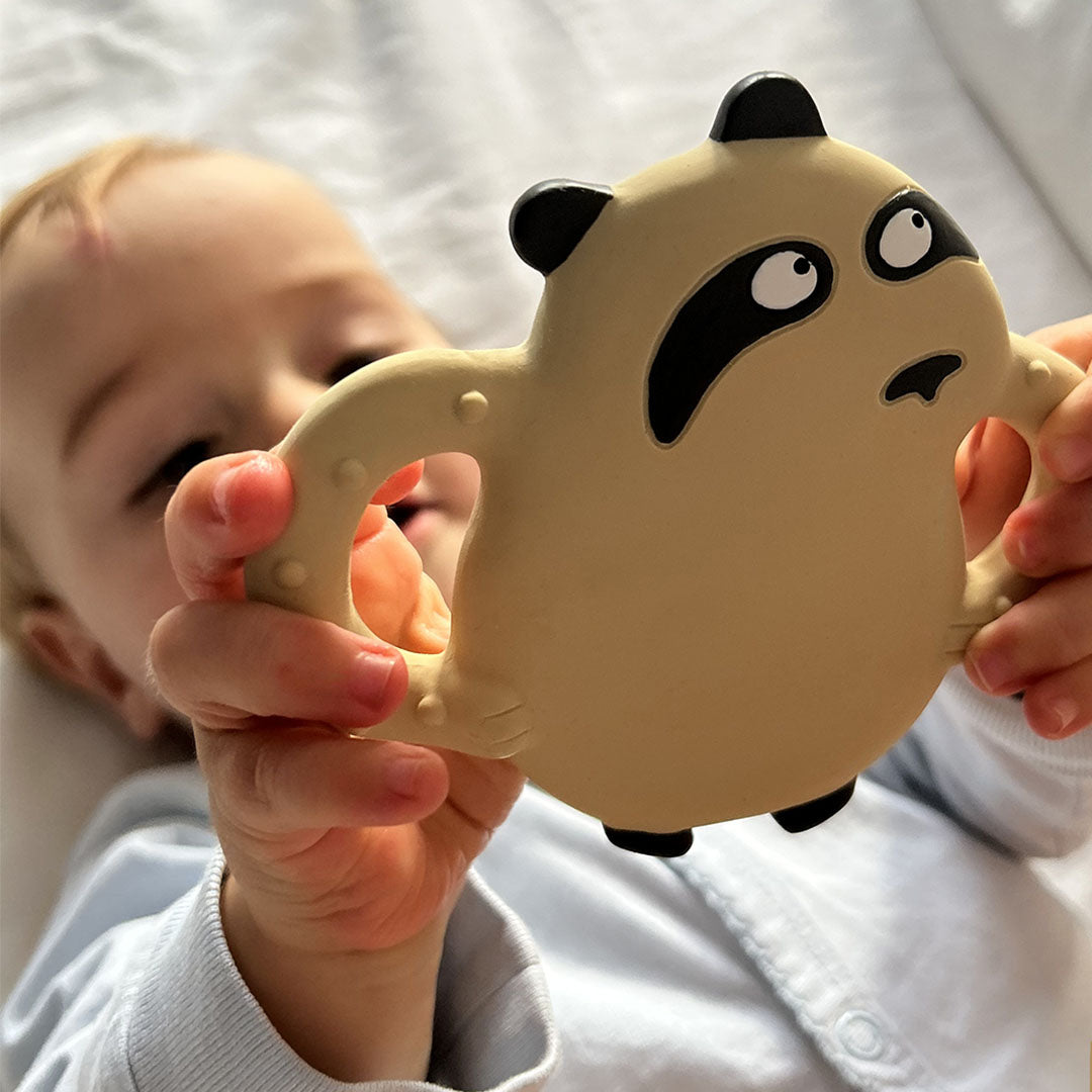Een baby houdt de Maison Petit Jour bijtring in de vorm van een beige panda vast.