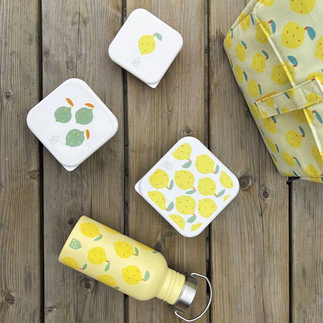 Bovenaanzicht van maison petit jour snackdoosjes, een waterfles en een lunchtas met citroenprint op een houten tafel.