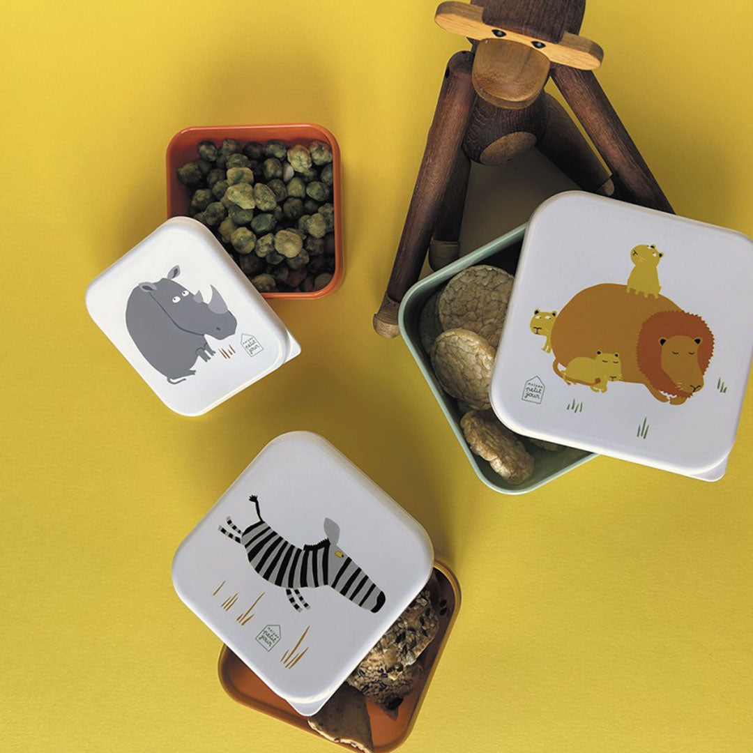 Drie Maison Petit Jour snackdoosjes met savannedieren, gevuld met verschillende snacks op een gele ondergrond.