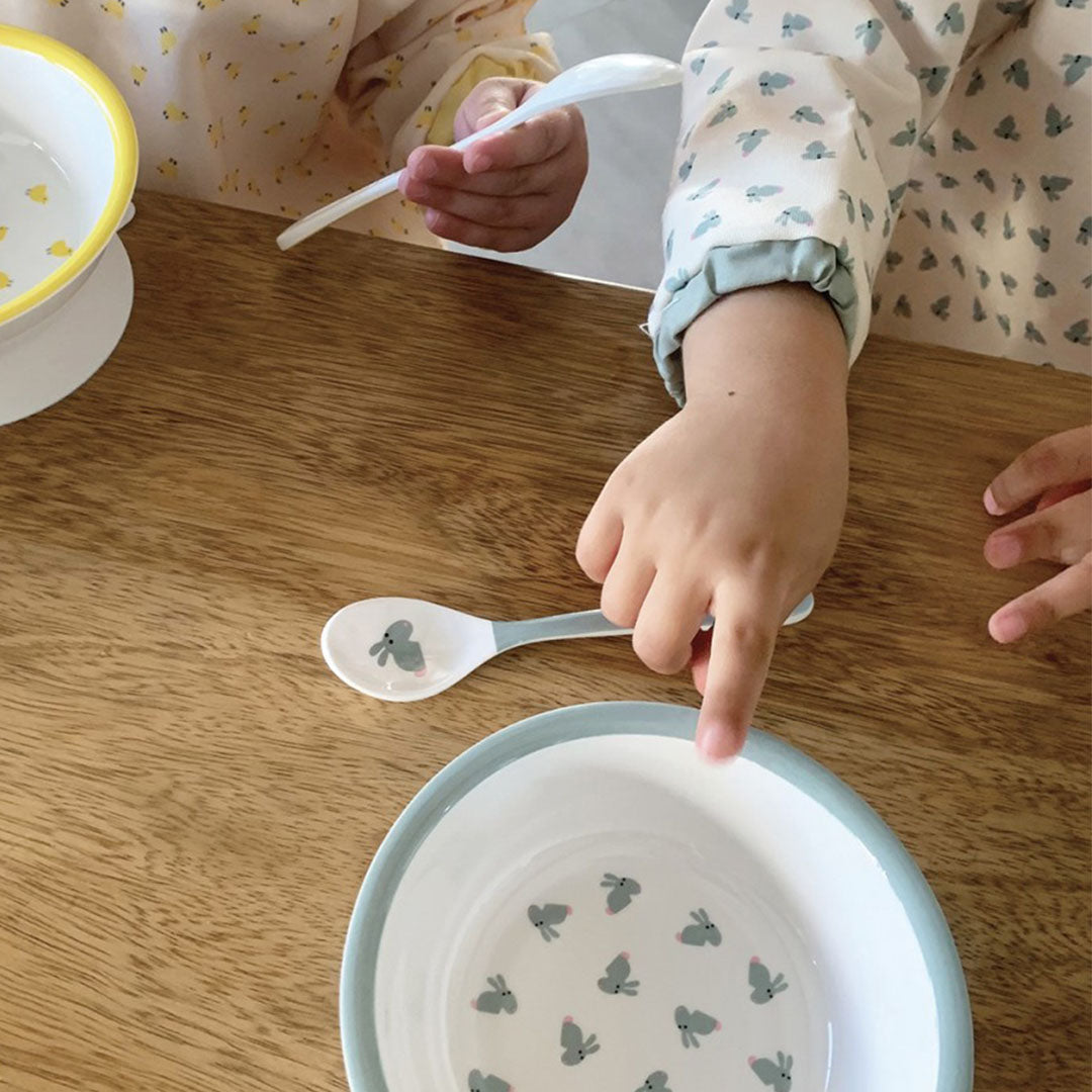 Een kind draagt een mouwslab met konijnenpatroon en wijst naar een bijpassende kom en lepel.