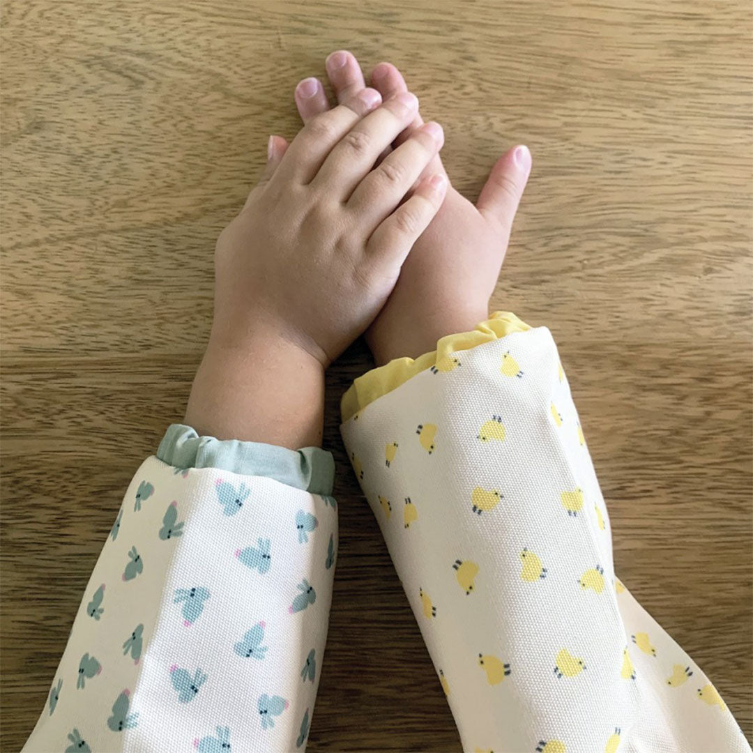 Twee kinderarmen dragen mouwslabs met verschillende dierenpatronen, de handen zijn gevouwen.
