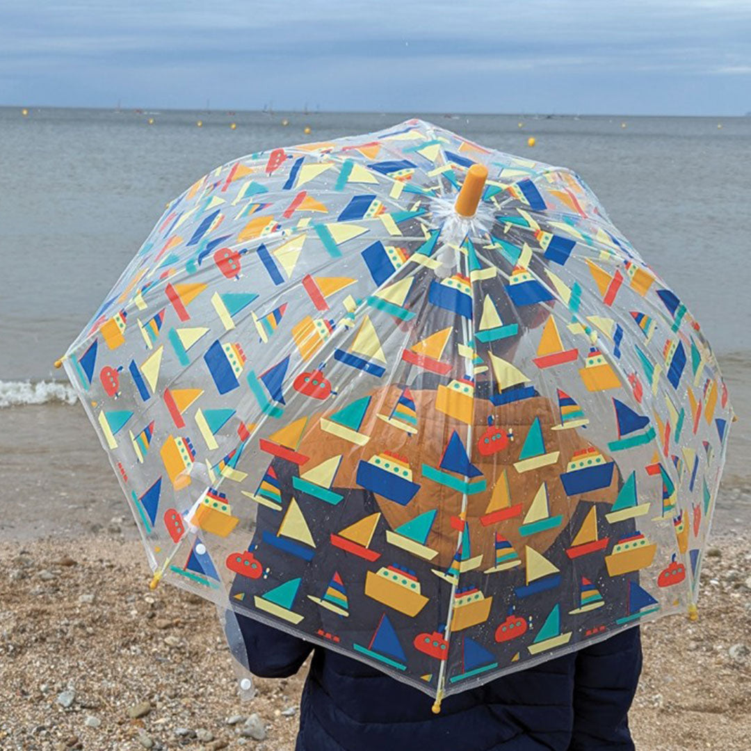 Kind met Maison Petit Jour kinderparaplu met botenpatroon op het strand.
