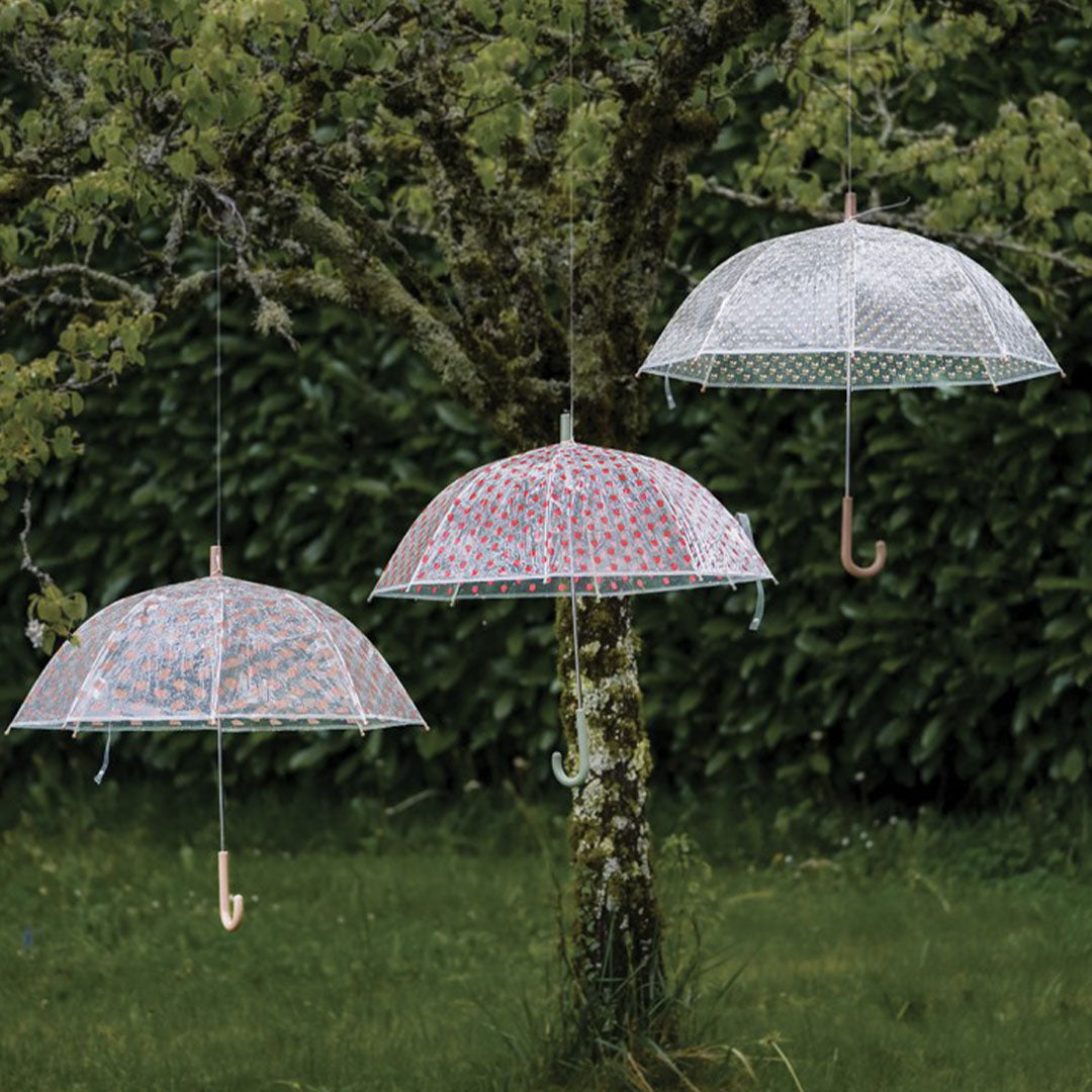 Drie Maison Petit Jour kinderparaplu's, waaronder een met egelpatroon, hangen in een boom.