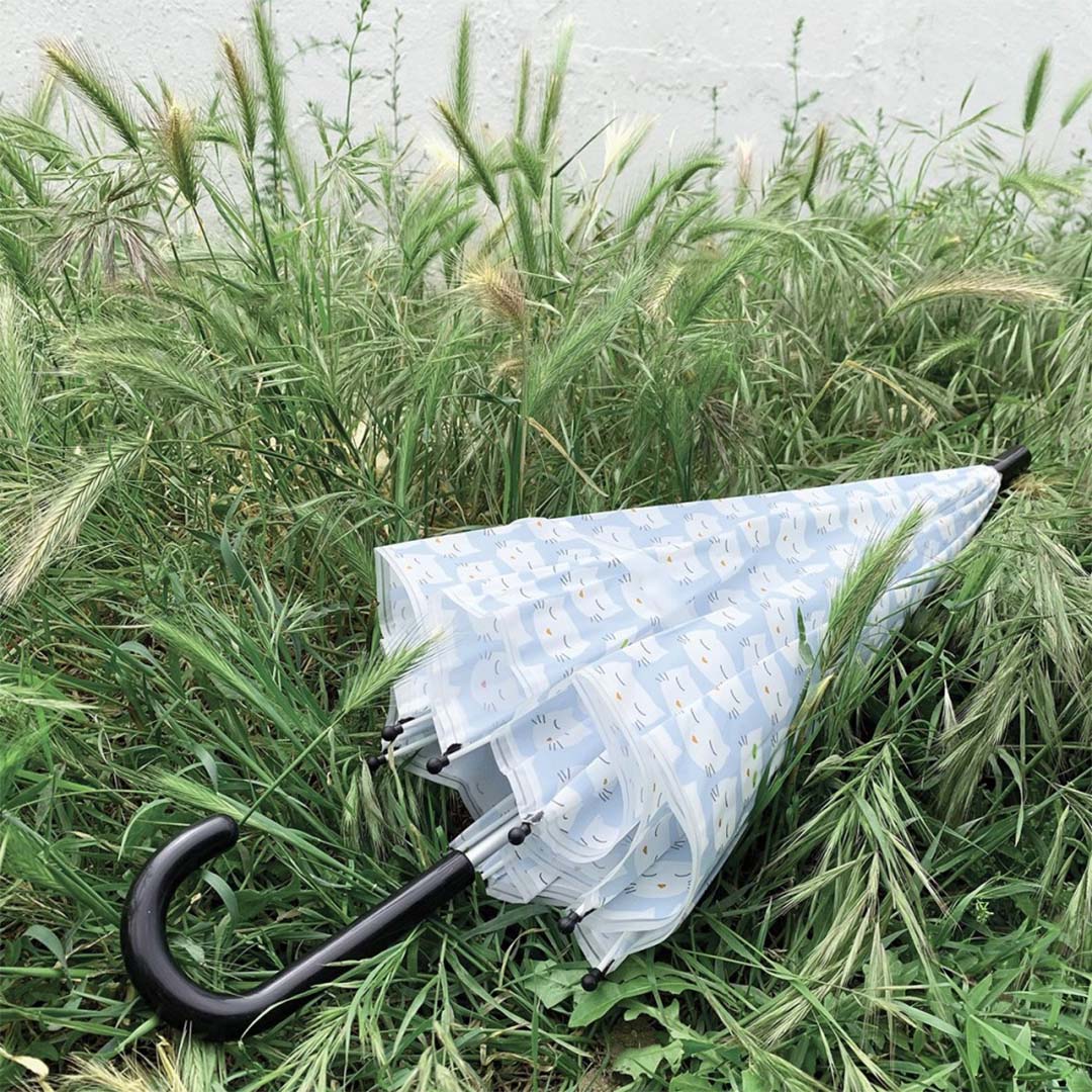 Maison petit jour kinderparaplu met kattenpatroon ligt gesloten in hoog groen gras.