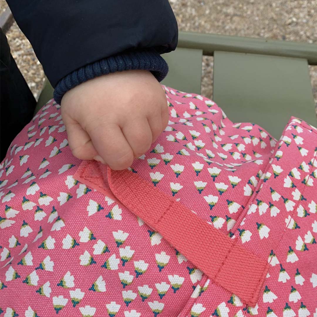 Een kinderhand houdt de sluiting van de roze kinderrugzak met bloemenpatroon vast.
