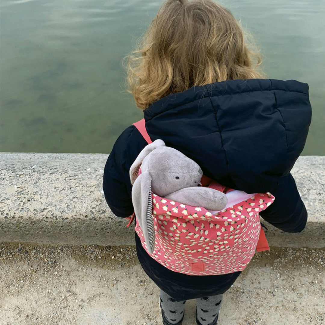 Een kind draagt de roze kinderrugzak met bloemenpatroon op de rug, met een knuffel erin.
