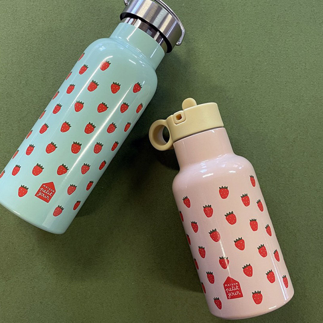 Twee Maison Petit Jour kinder drinkflessen met aardbeienprint, een roze en een lichtblauwe, op een groene ondergrond.
