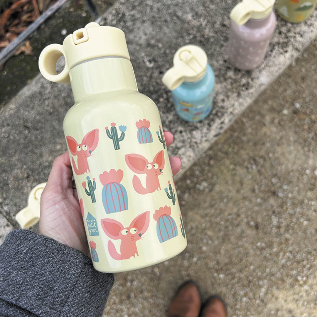Een hand houdt de Maison Petit Jour rvs drinkfles met vossen en cactussen vast, buiten op een stoep.