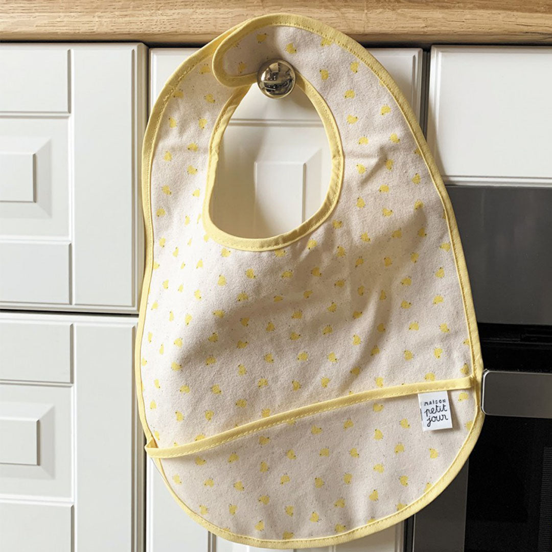 Maison petit jour babyslab met geel kuikenpatroon hangend aan een haakje op witte keukenkastjes.