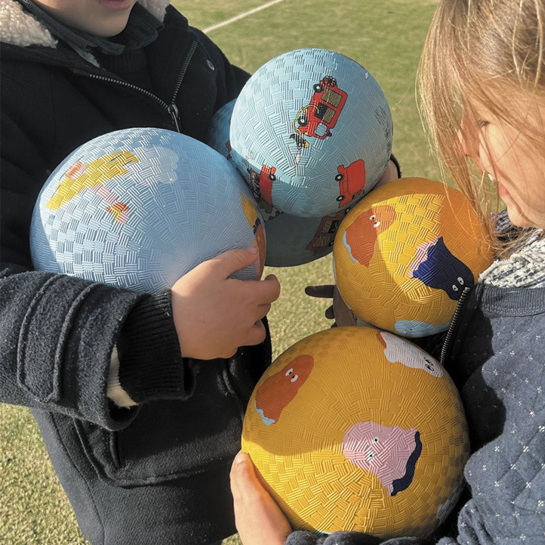 Twee kinderen houden meerdere Maison petit jour speelballen vast, waaronder een blauwe met brandweerwagens en gele ballen met andere patronen.