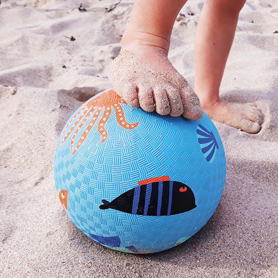 Kindervoet op een Maison petit jour blauwe speelbal met zeedieren op het strand.