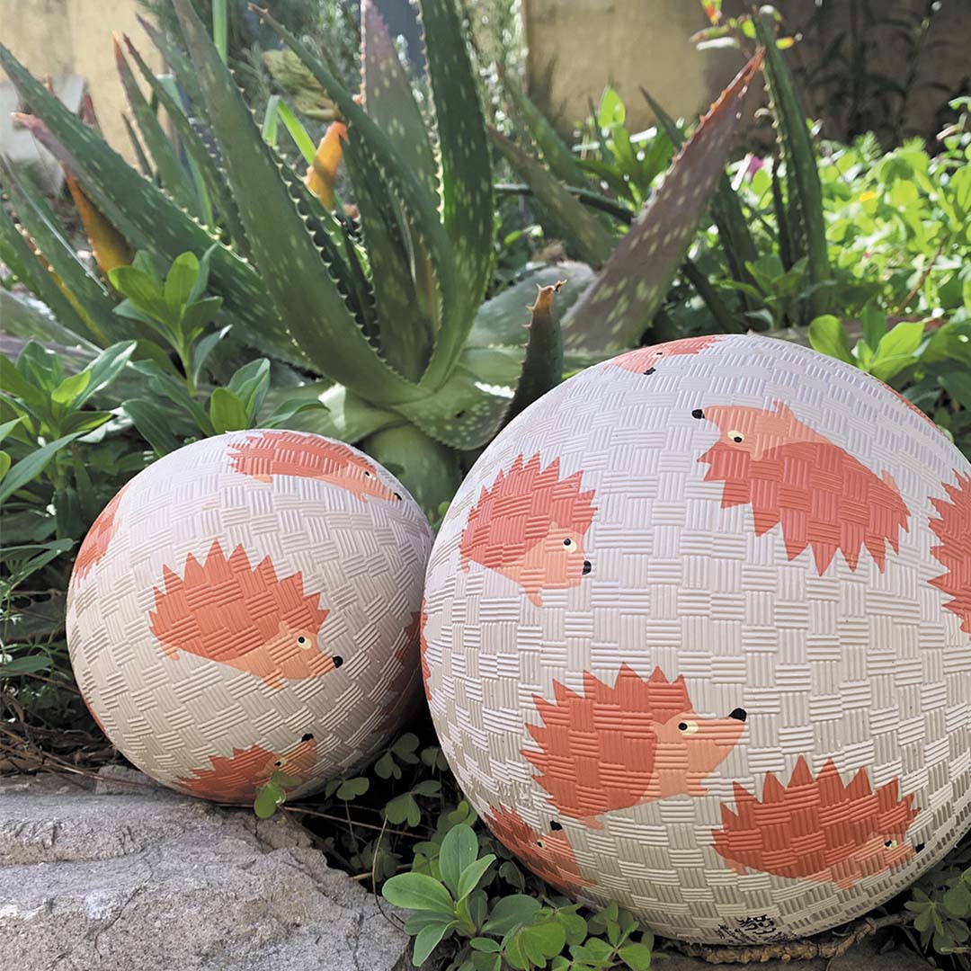 Twee speelballen van Maison Petit Jour met egelpatroon in een tuin.