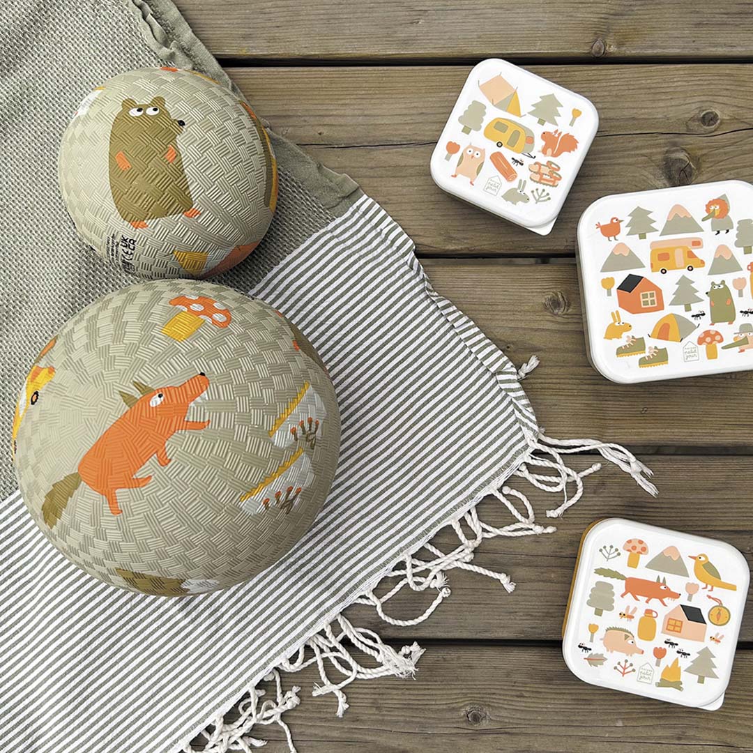 Twee Maison Petit Jour speelballen en drie bijpassende lunchboxen met avontuurlijke dierenpatronen op een houten ondergrond.