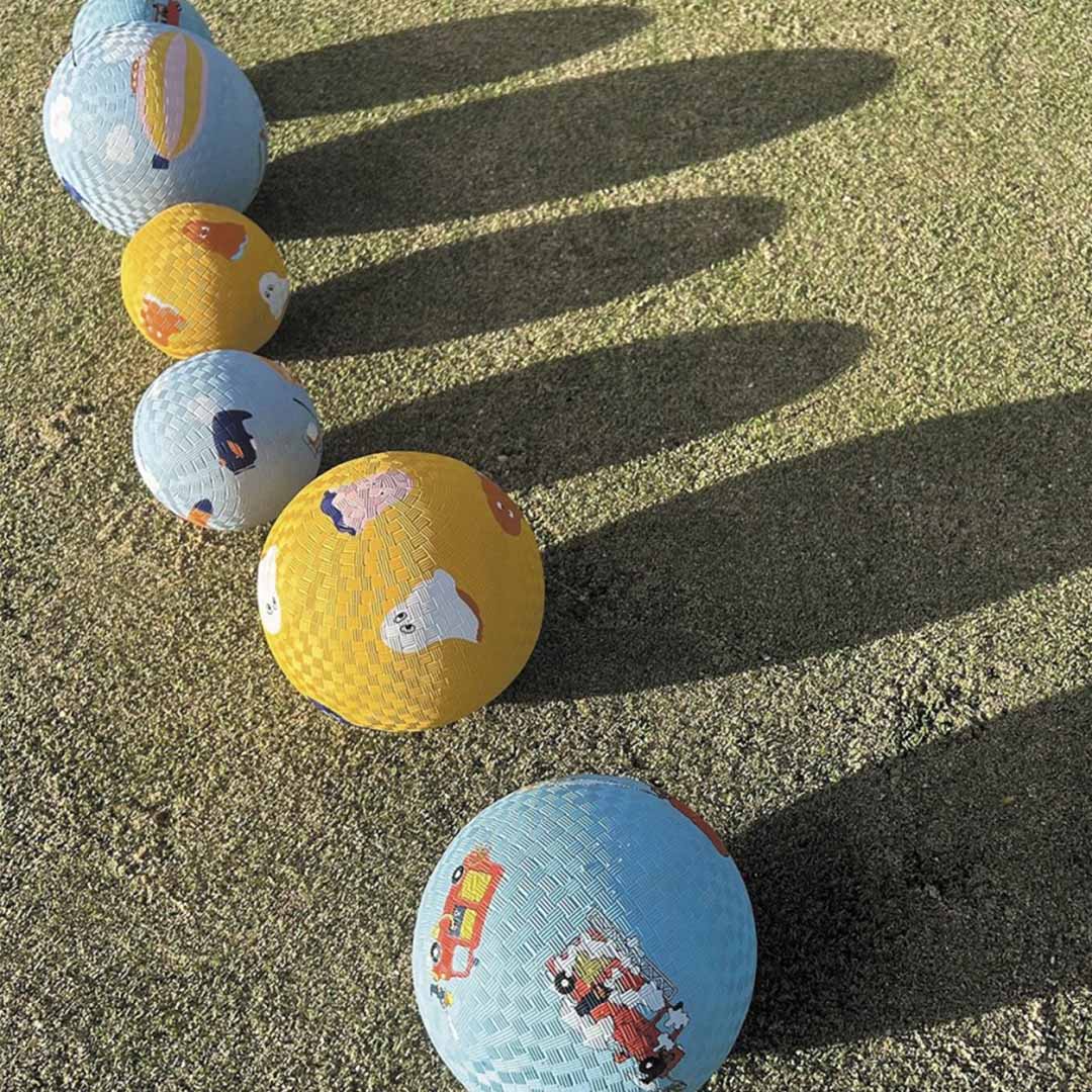 Rij van maison petit jour speelballen met spookjes en voertuigen op een grasveld met lange schaduwen.