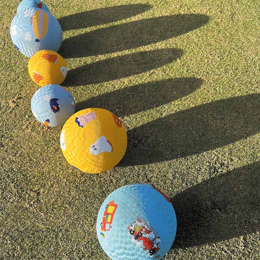 Een rij van vijf maison petit jour speelballen op het gras, afwisselend gele met spookjes en blauwe met voertuigen.