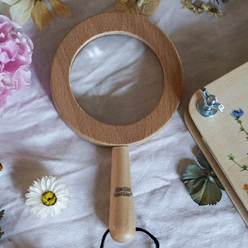 mama memo houten vergrootglas liggend op een doek, omringd door gedroogde bloemen en een bloemenpers.