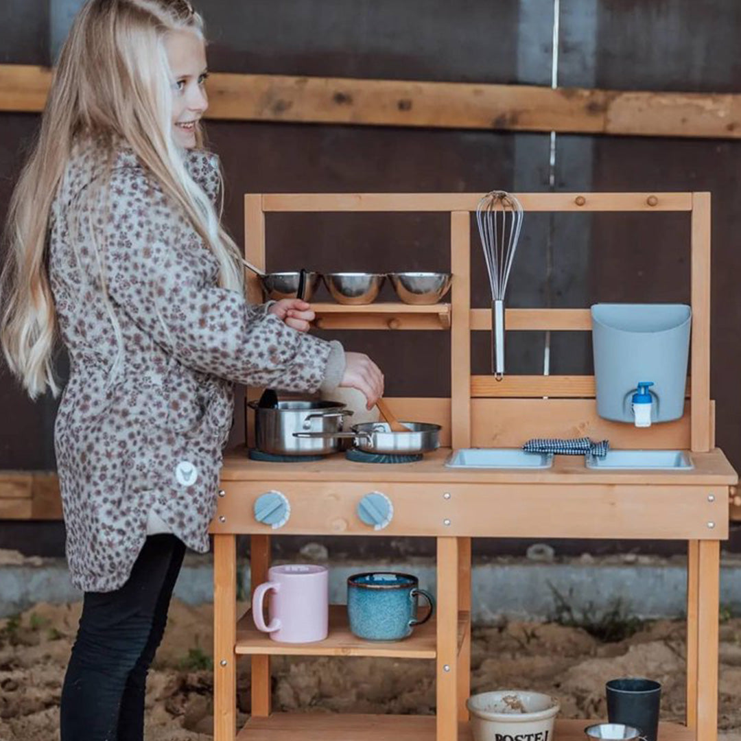 Een lachend kind roert in een pan op de mama memo houten kinder buitenkeuken.
