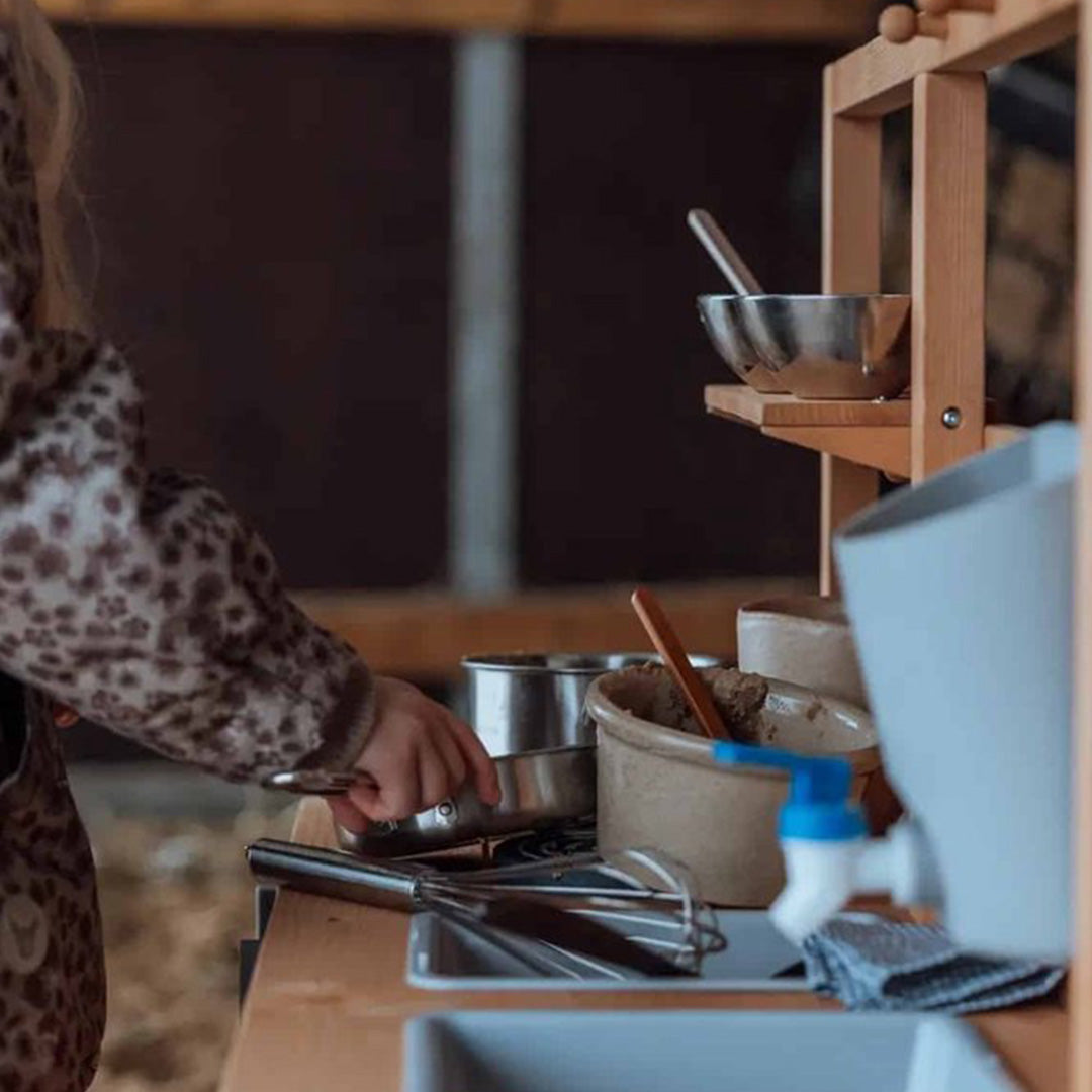 Detail van kinderhanden die spelen met potten en een garde op de mama memo houten buitenkeuken.
