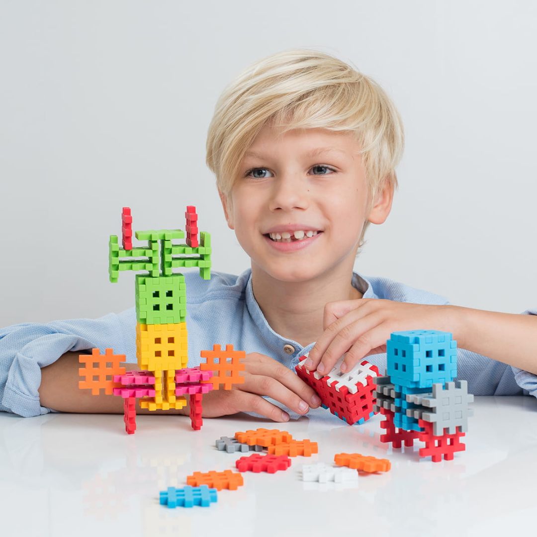 Een lachende jongen speelt met kleurrijke Marioinex Mini Waffle bouwblokken en gemaakte figuren.