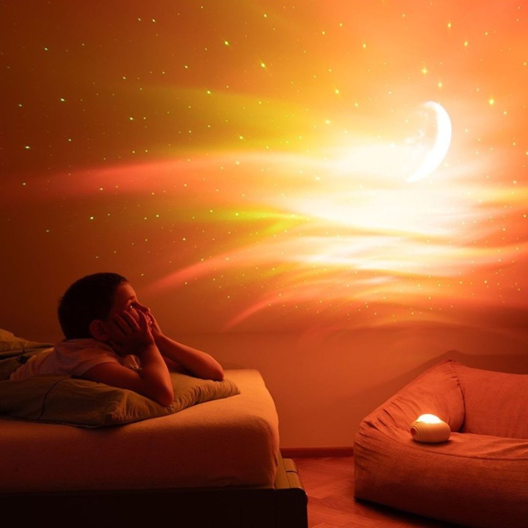 Kind kijkt naar een muur verlicht met oranje en gele aurora, sterren en een maan, geprojecteerd door de mary's lichtprojector.