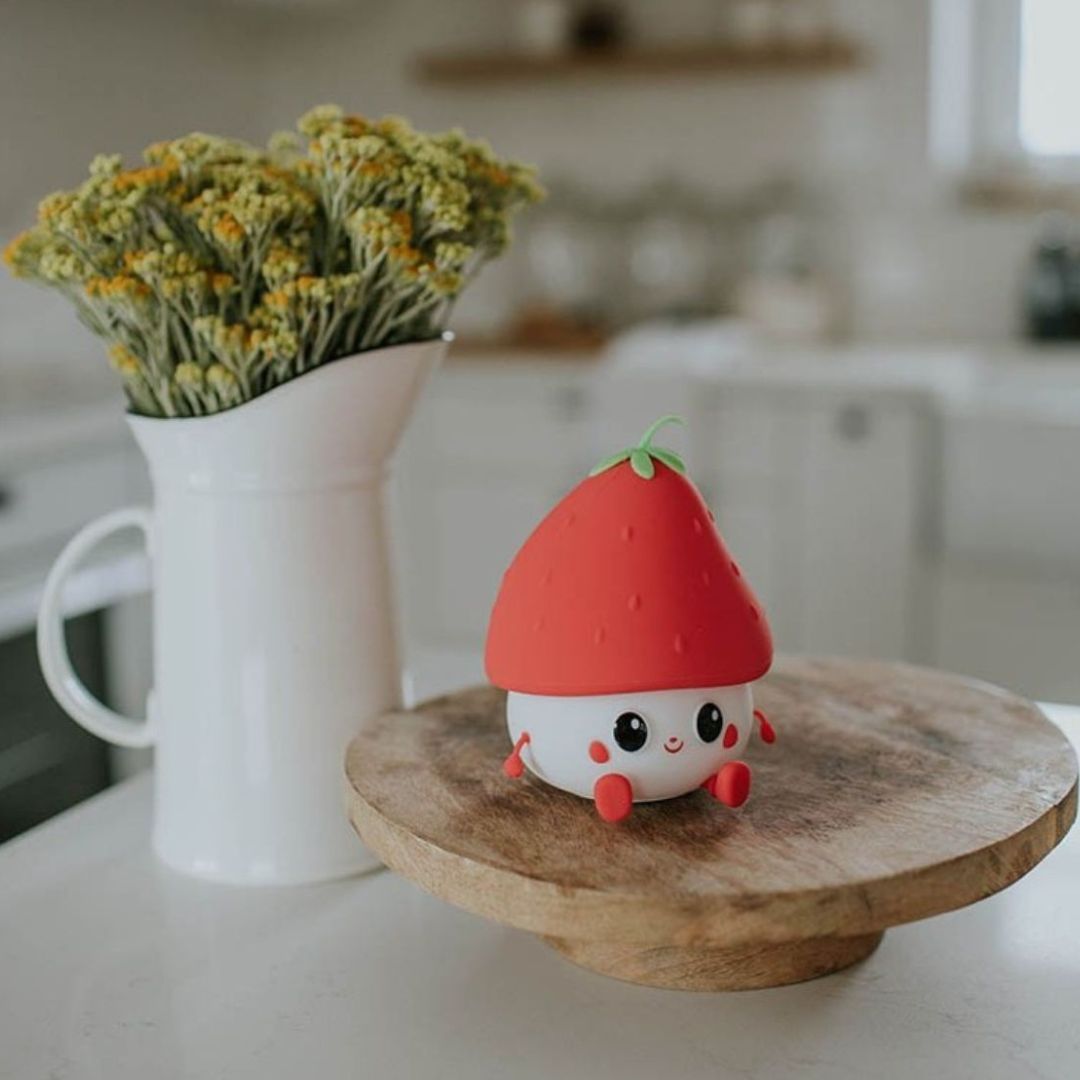 Een aardbei nachtlampje staat op een houten plateau naast een vaas met bloemen.