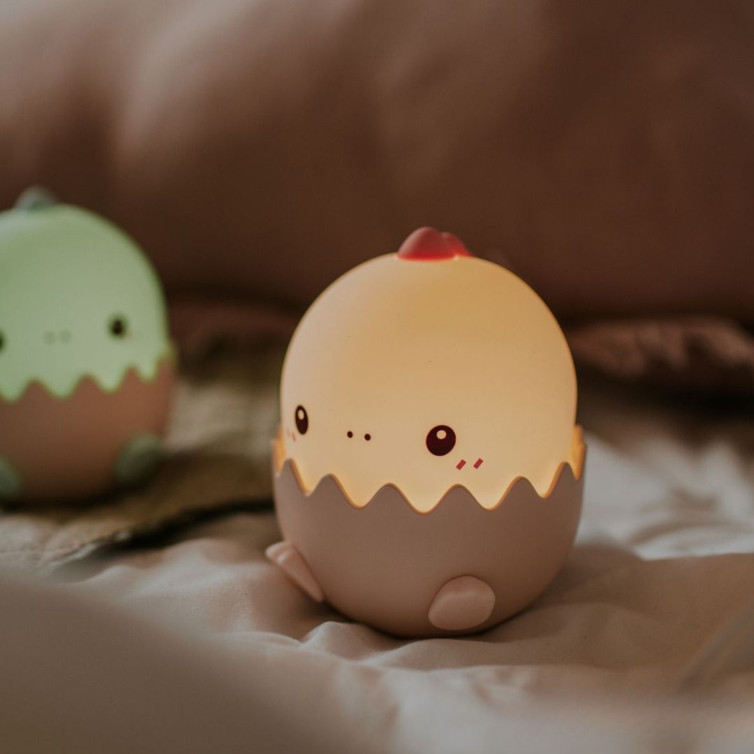 Een mary's baby dino nachtlampje dat warm wit licht geeft op een bed.