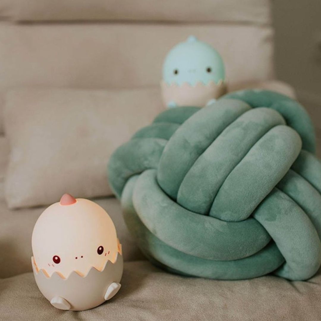 Een mary's baby dino nachtlampje naast een groen kussen op een bed.