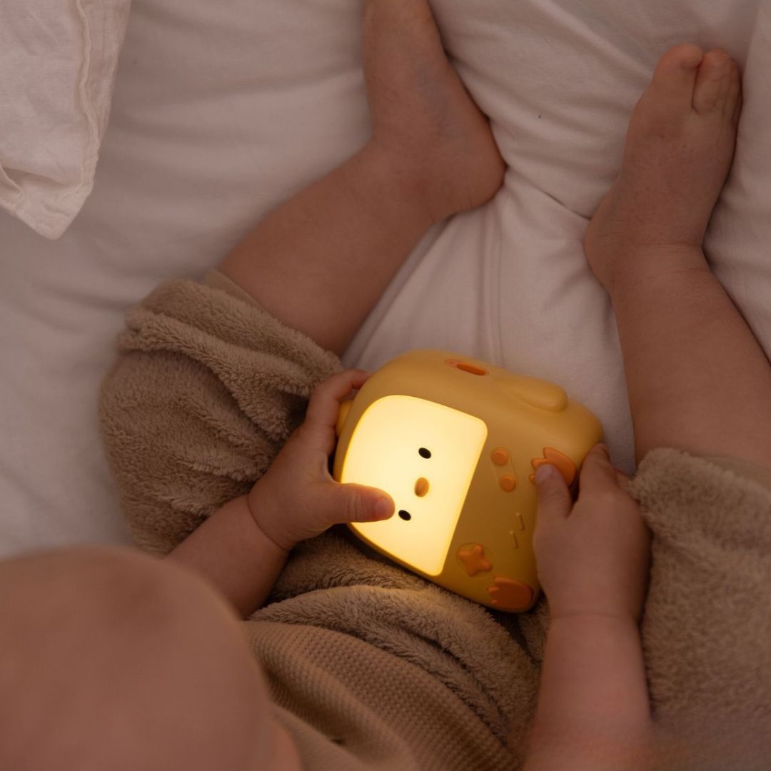 Een baby houdt het oplichtende mary's gele kuiken nachtlampje vast in bed.