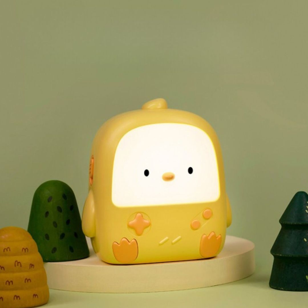 Het mary's gele kuiken nachtlampje staat aan en geeft warm wit licht, omringd door decoratieve boompjes.