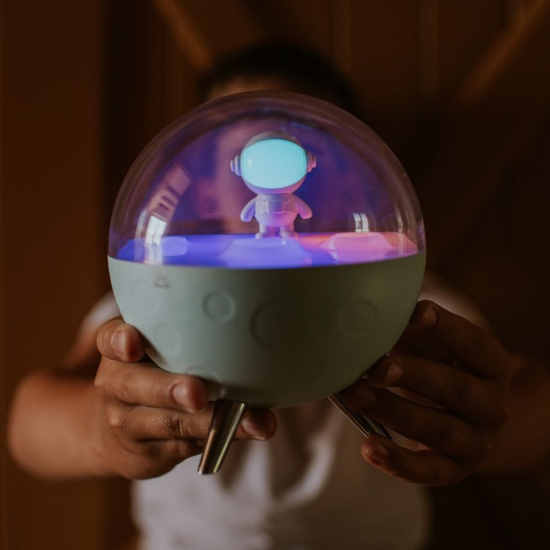 Een persoon houdt het Mary's nachtlampje maan met astronautfiguur en paars licht vast.