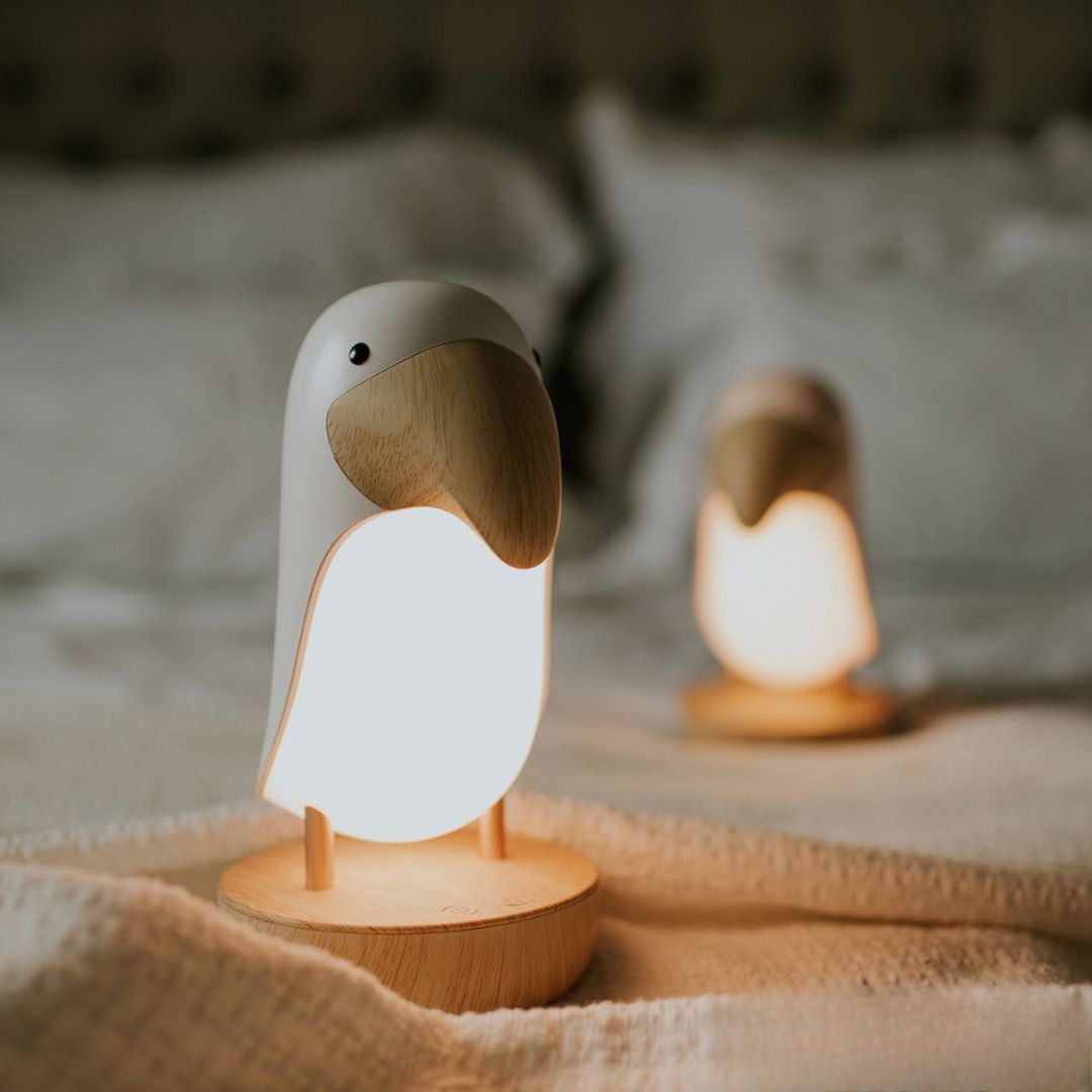 Mary's toekan nachtlampje geeft warm wit licht op een bed.