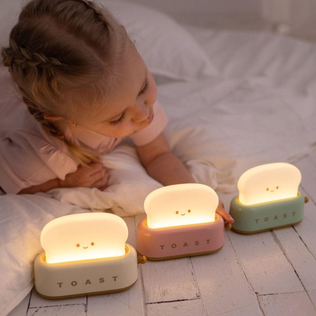 Een kind kijkt naar drie oplichtende Mary's toaster nachtlampjes in roze, wit en mintgroen.