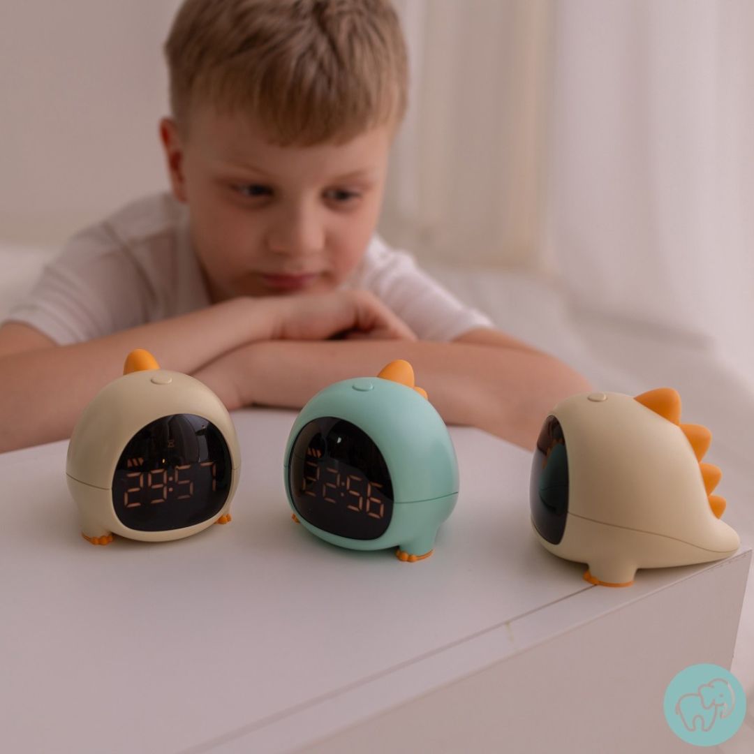 Een jongen kijkt naar drie dino wekkers in geel en blauw.