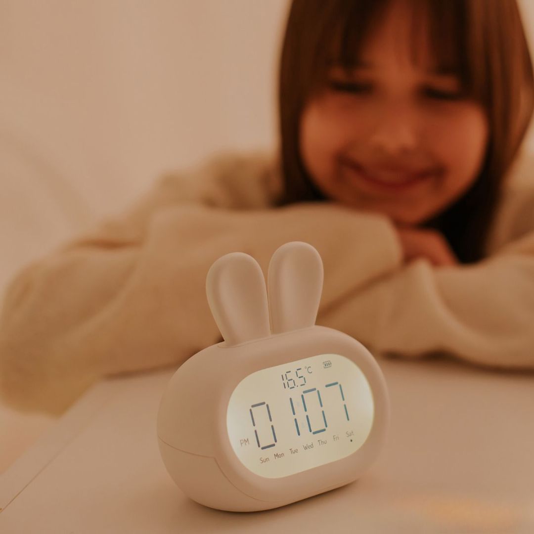 Mary's witte kinderwekker in konijnvorm met digitale tijd en temperatuur, met een kind op de achtergrond.