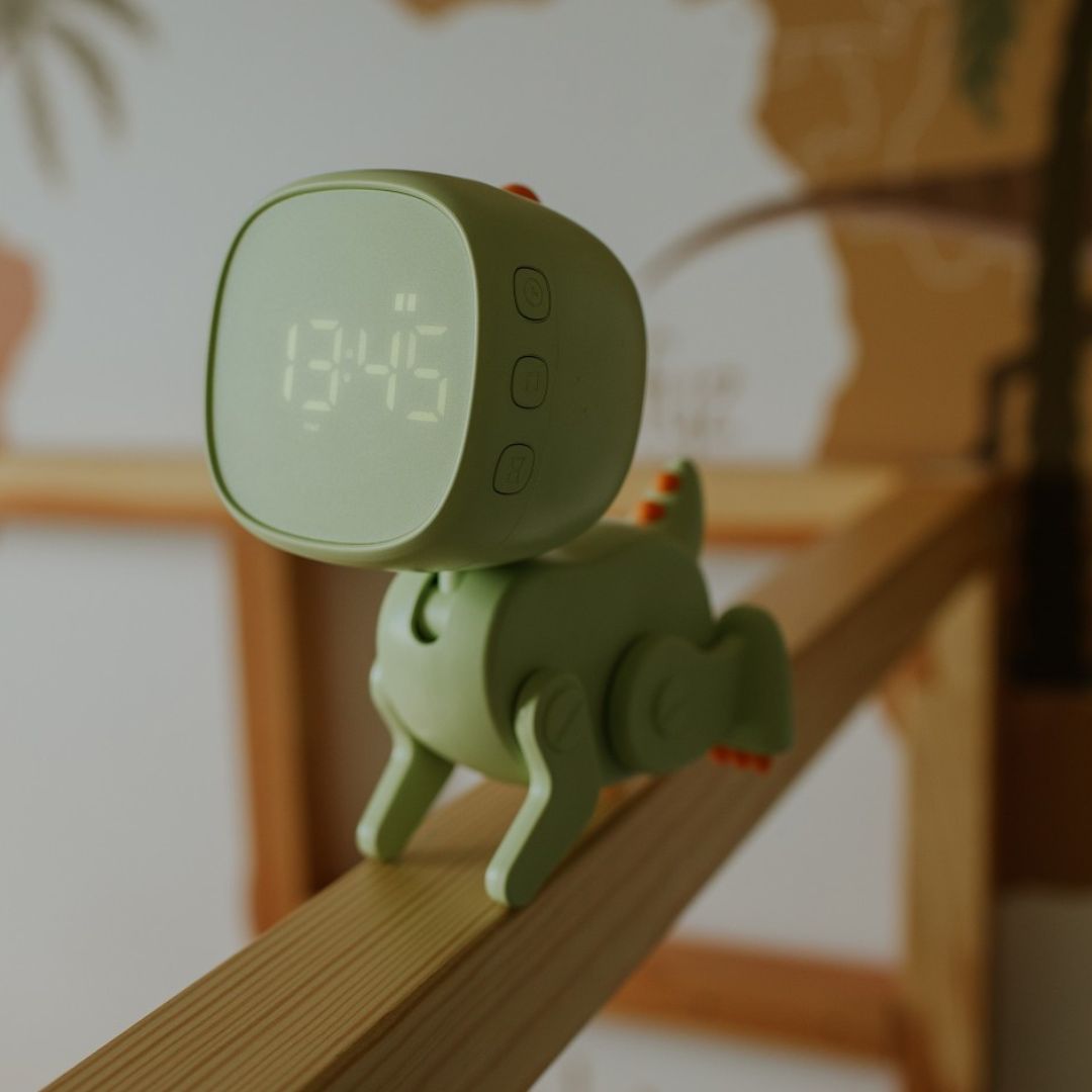 Groene robot dino wekker met digitale tijd 13:45, liggend op een houten plank.