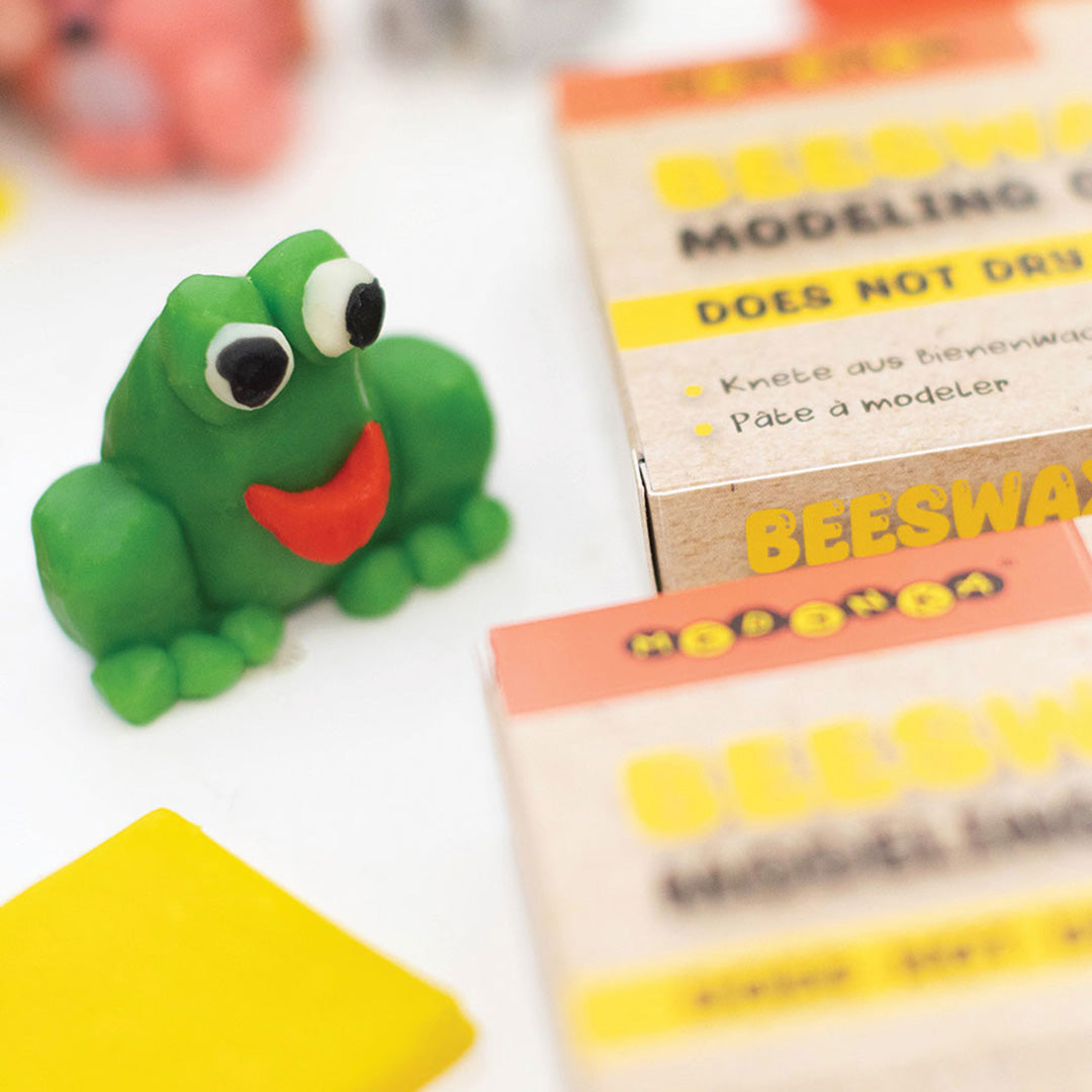 Een groen kleifiguur van een kikker, gemaakt met Medenka bijenwas modelleerklei, naast de verpakking.
