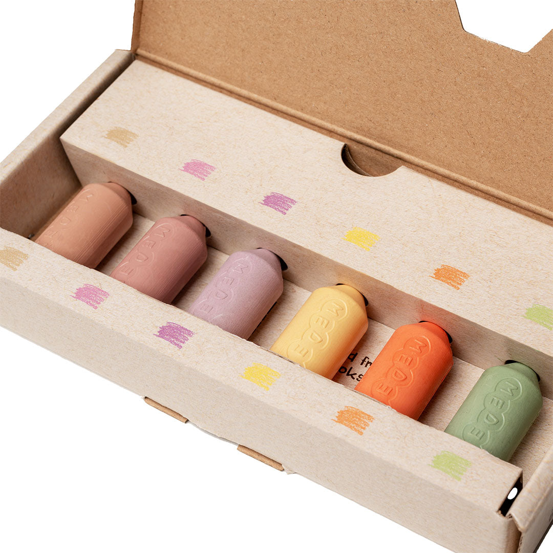 Zes Medenka bijenwaskrijtjes in pastelkleuren liggen in hun open kartonnen verpakking.