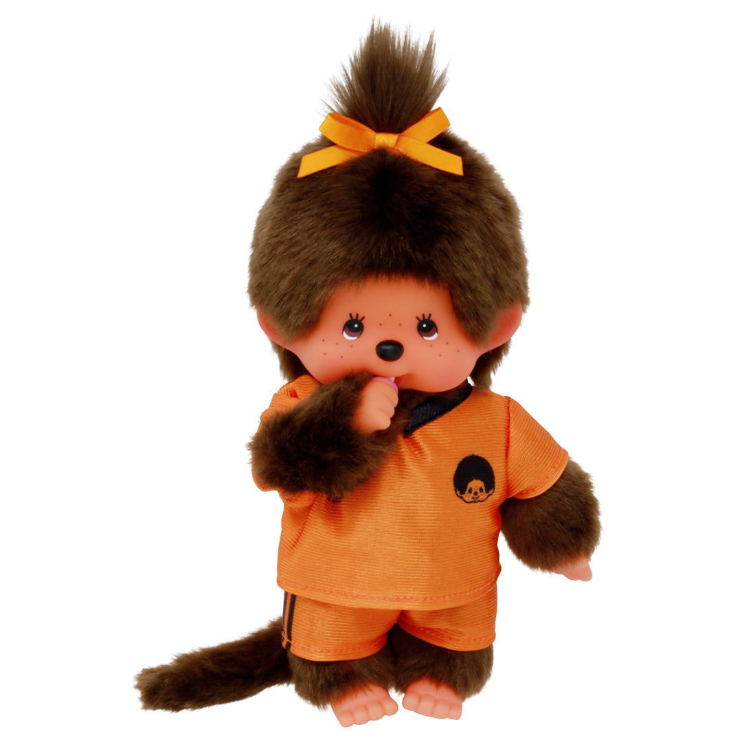 Monchhichi pop meisje in oranje voetbaltenue met de duim in de mond.