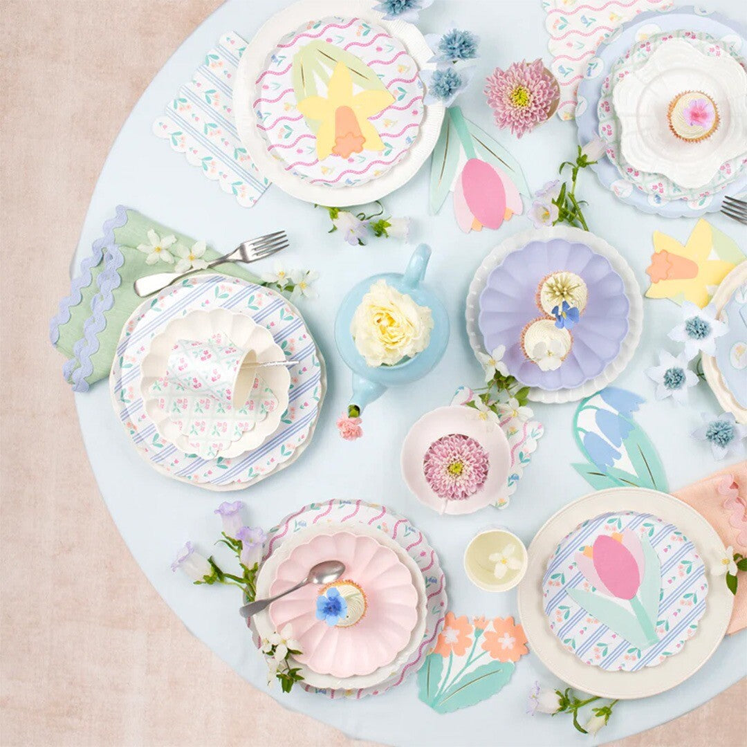 Een Meri Meri feesttafel met borden, bekers en decoraties met bloemen en lentethema.