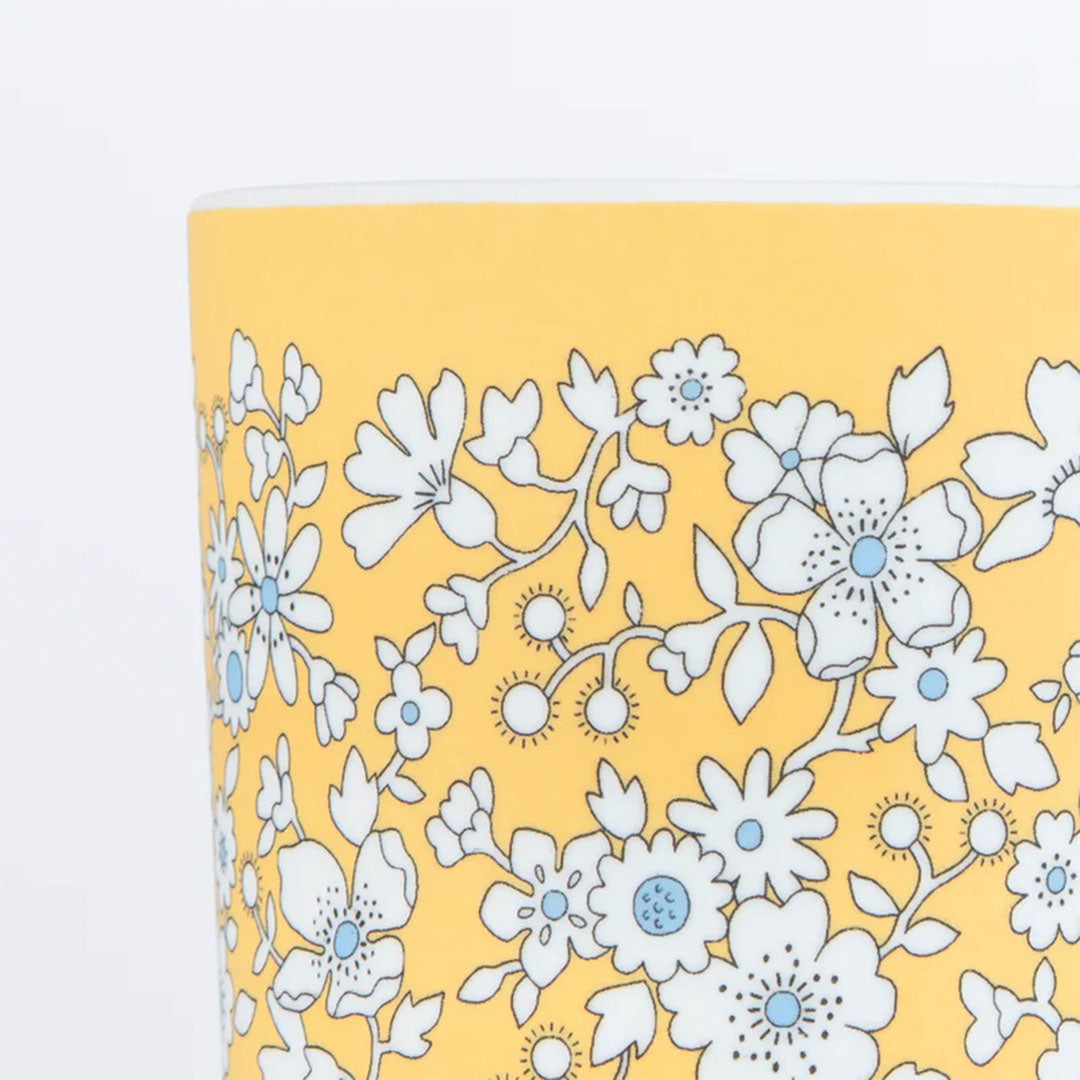 Detail van een gele beker met een wit en lichtblauw bloemenpatroon.