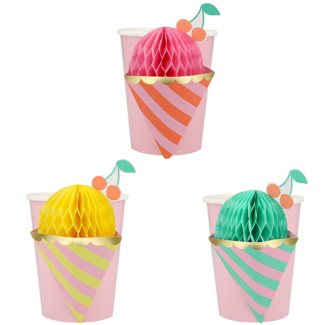 Drie Meri Meri feestbekers in de vorm van ijshoorntjes met roze, gele en groene honingraatdecoraties en kersen.