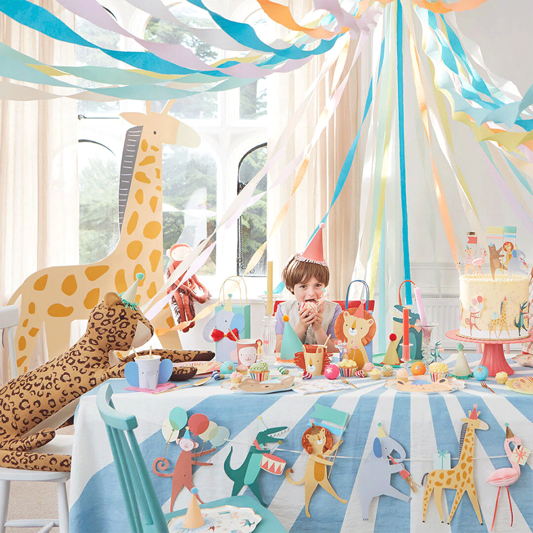 Een kind zit aan een feestelijk gedekte tafel met dierenthema, versierd met slingers en feestartikelen.