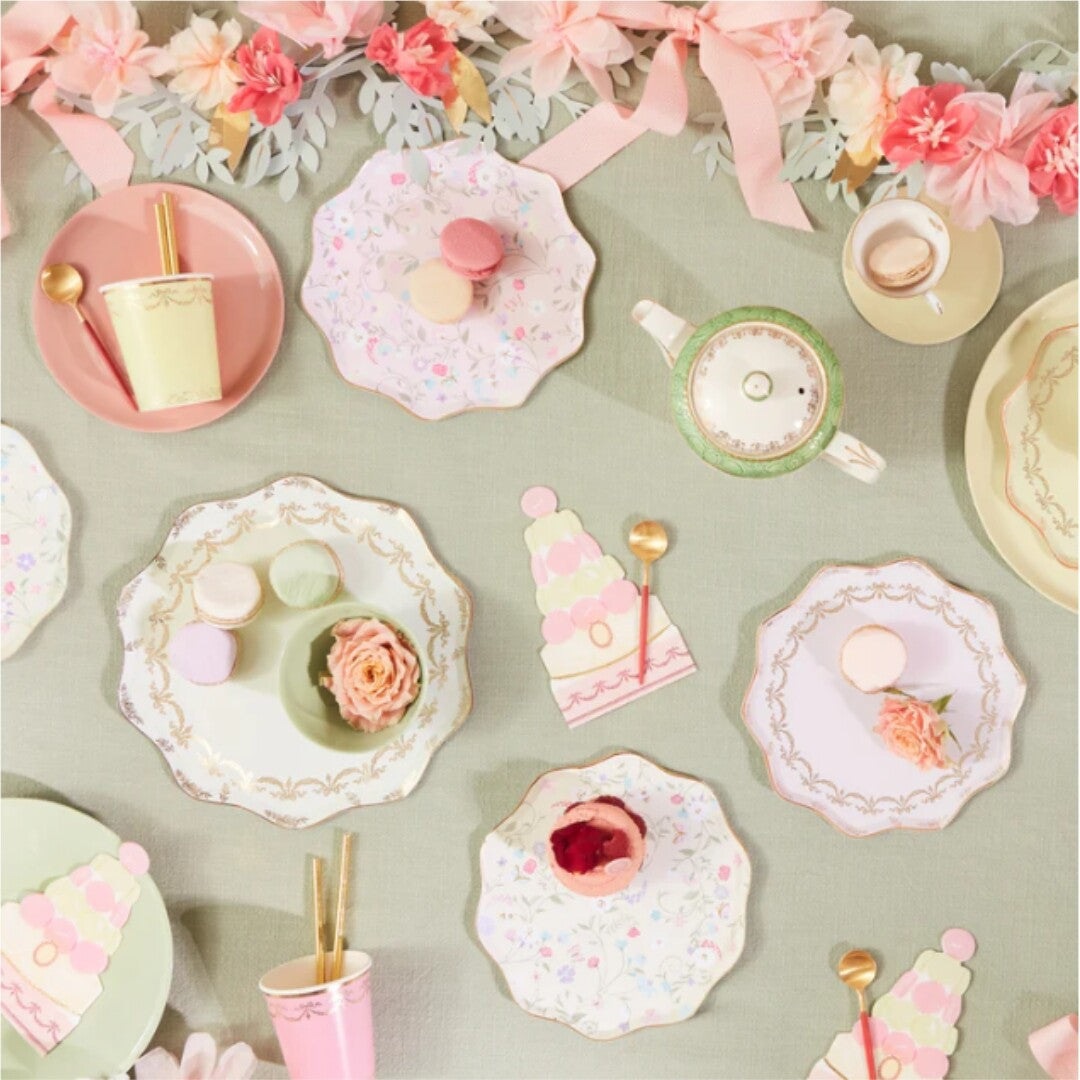 Een feestelijk gedekte tafel met Meri Meri papieren borden, bekers en desserts, versierd met een bloemenguirlande.