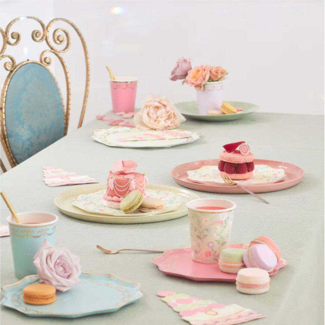 Een gedekte tafel met Meri Meri papieren feestborden en bekers in pastelkleuren, met desserts en bloemen.