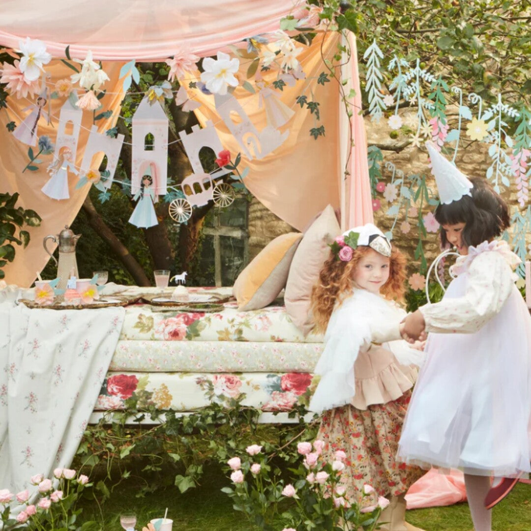 Twee meisjes verkleed als prinsessen spelen in een feestelijk versierde tuin.