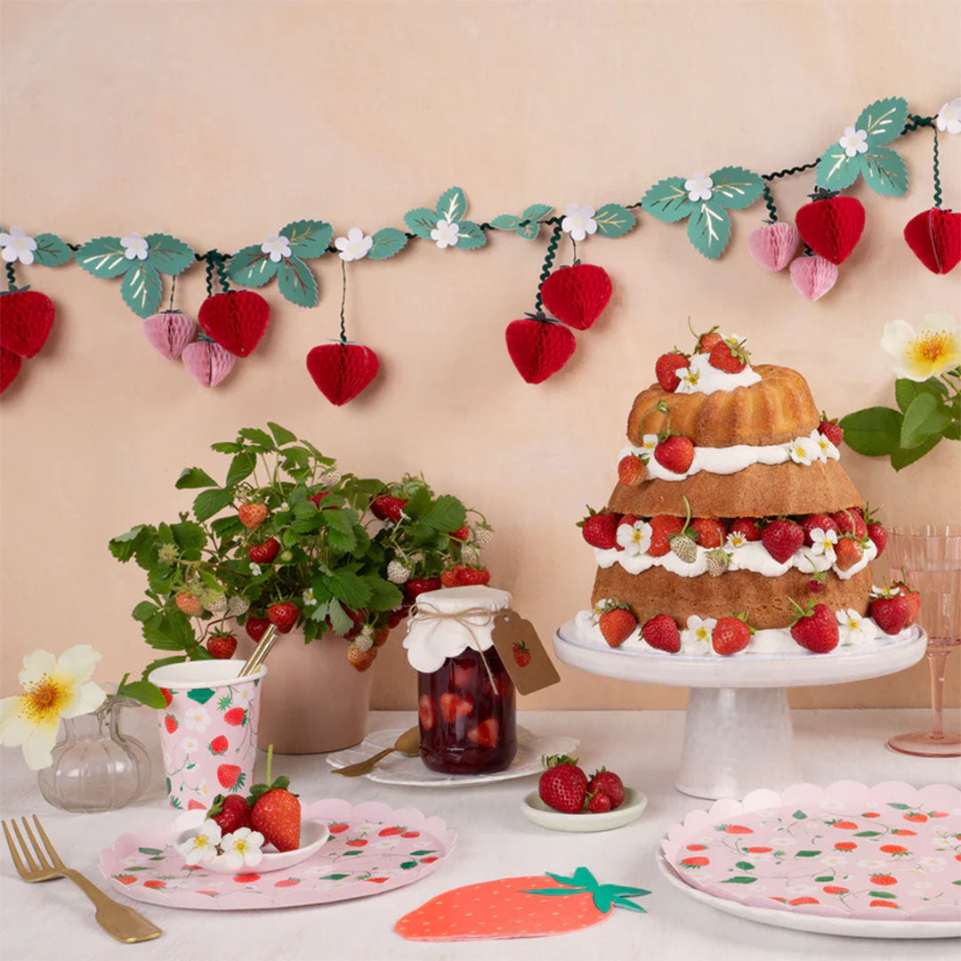 Een feestelijk gedekte tafel met Meri Meri aardbeien thema feestartikelen, een taart en decoraties.