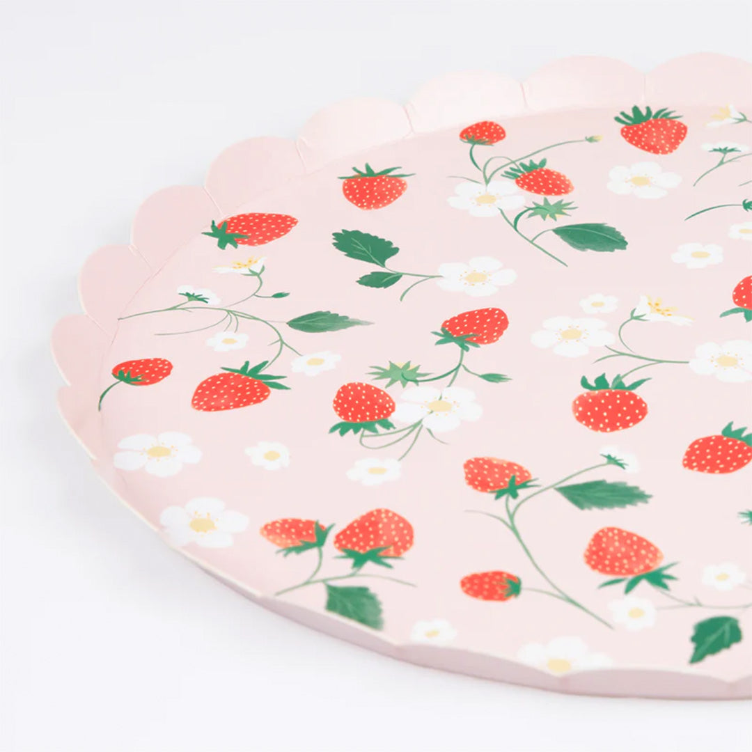 Detail van een roze papieren bord met geschulpte rand en een patroon van aardbeien, bladeren en witte bloemen.