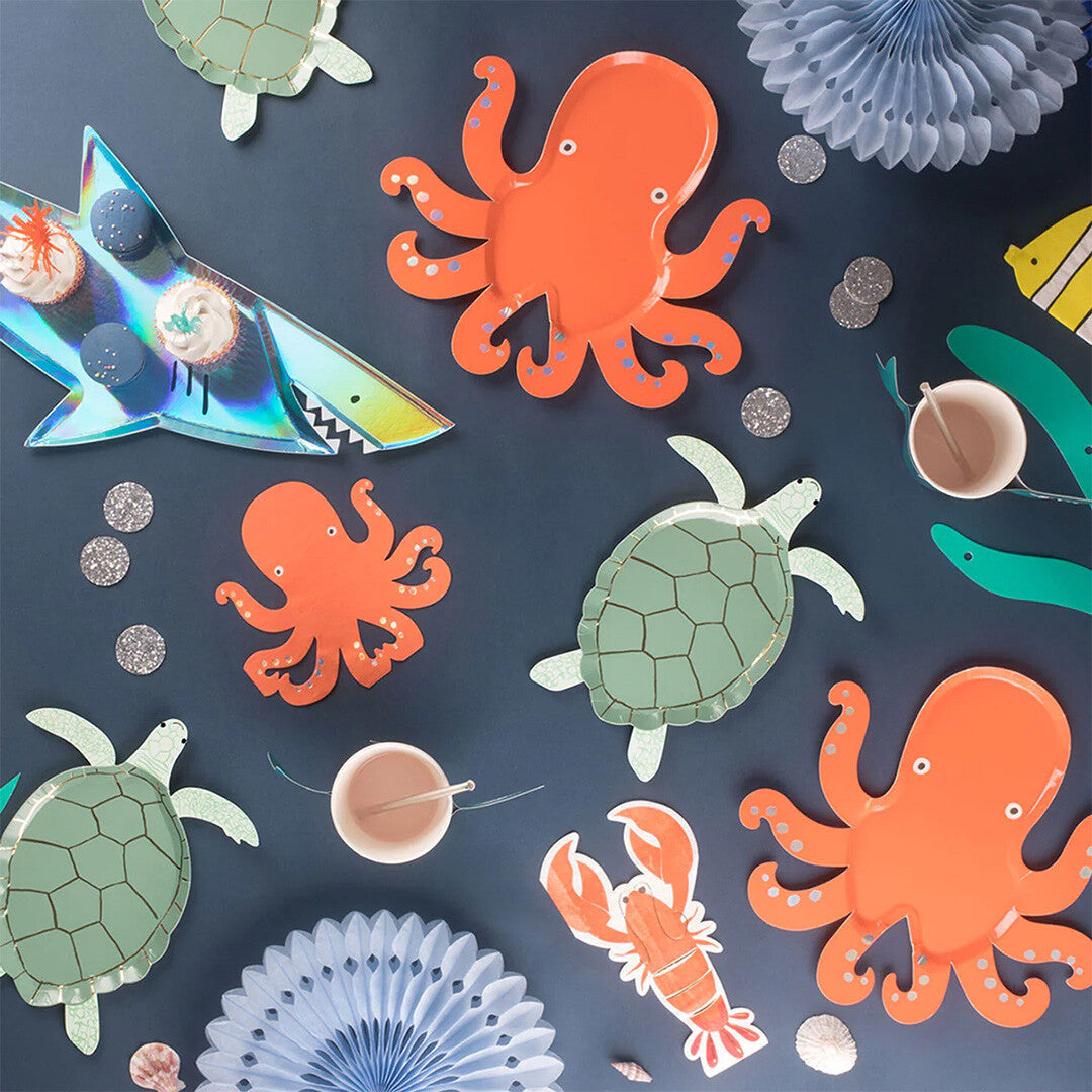 Een overzicht van Meri Meri feestartikelen met onderwaterthema, waaronder oranje octopus bordjes en groene schildpad bordjes.