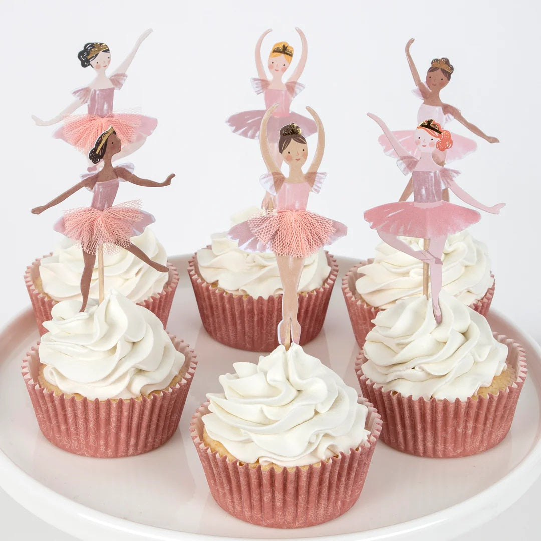 Zes versierde cupcakes met witte frosting en Meri Meri ballerina cupcake toppers in roze vormpjes.