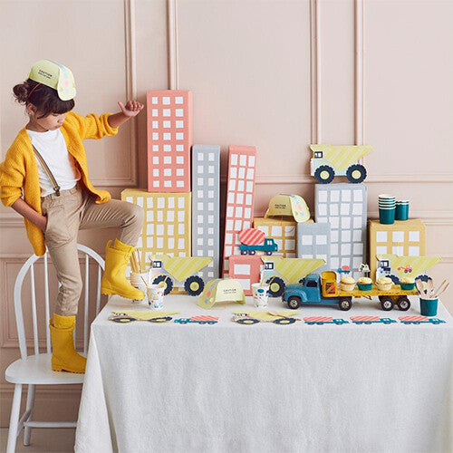 Een kind bij een feestelijk gedekte tafel met Meri Meri bouwthema decoraties en cupcakes.